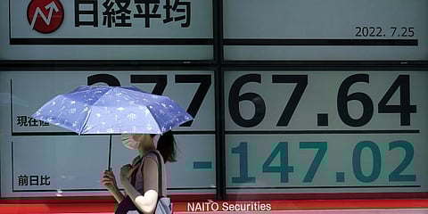A person wearing a protective mask walks in front of an electronic stock board showing Japan's Nikkei 225 index at a securities firm on Monday. (Photo | AP)