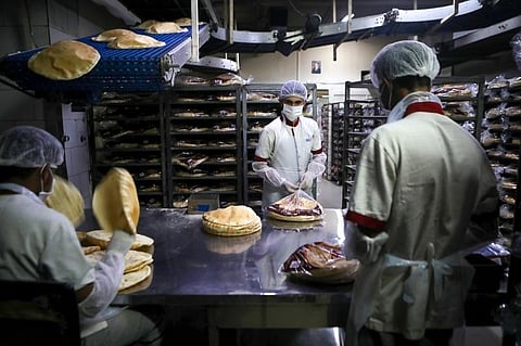 Employees, wearing personal protective equipment, pack bread at a bakery in the Lebanese capital Beirut. (File Photo | AFP)