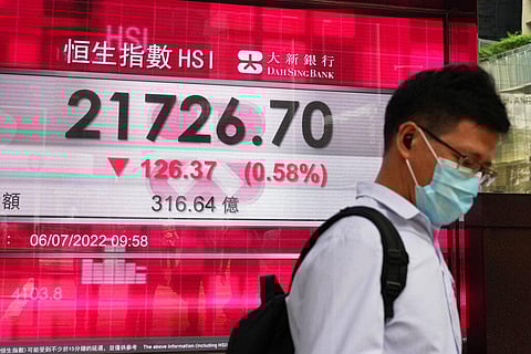 A man wearing a face mask walks past a bank's electronic board showing the Hong Kong share index in Hong Kong, Wednesday, July 6, 2022.(Photo | AP)