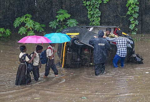 Students walk past as others try to repair an auto-rickshaw on a flooded road amid heavy monsoon rains, in Mumbai. (Photo | PTI)
