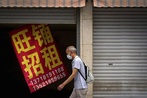 A man wearing a face mask walks by a banner that reads 'Prosperous shop for rent' hangs on a vacant shop lot in Beijing. (Photo | AP)
