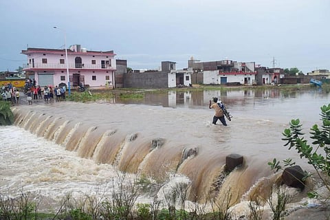 People wade through a flooded bridge near submerged houses after heavy rainfall in Satna, Madhya Pradesh, mid-August, 2022. (Photo | PTI)