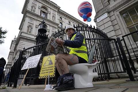 An activist sits on a toilet at the entrance to Downing Street to protest against raw sewage dumping in the rivers and seas around the UK. (Photo | AP)