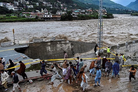 People gather in front of a road damaged by flood waters following heavy monsoon rains in Madian area in Pakistan's northern Swat Valley on August 27, 2022. (Photo |AFP)