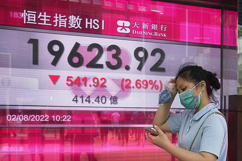 A woman wearing a face mask walks past a bank's electronic board showing the Hong Kong share index in Hong Kong, Tuesday, Aug. 2, 2022.(Photo | AP)
