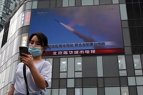 A woman uses her mobile phone as she walks in front of a large screen showing a news broadcast about China's military exercises encircling Taiwan, in Beijing on Thursday. (Photo | AFP)