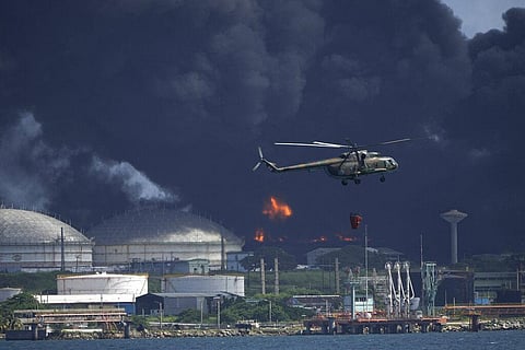 A helicopter carrying water flies over the Matanzas Supertanker Base, as firefighters try to quell the blaze which began during a thunderstorm the night before, in Matazanas, Cuba. (Photo | AP)