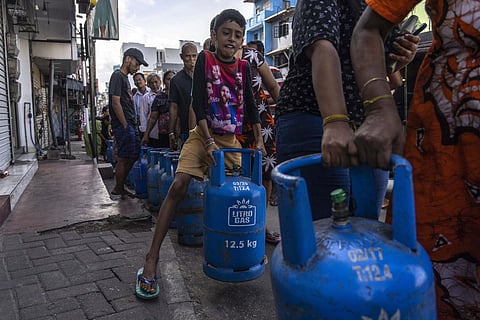 A boy tries to lift an empty cylinder as he along with others wait in a queue to buy domestic gas at a distribution centre, in Colombo, Sri Lanka. (File Photo | AP)