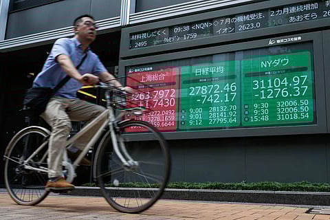 A man cycles past a sign (C) showing the numbers on the Nikkei-225 stock index and the New York Stock Exchange (R) in Tokyo. (AFP)