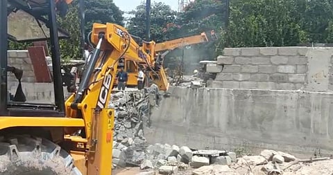 An excavator demolishes the compound wall built on a drain at Doddakannelli. (Photo | Express)