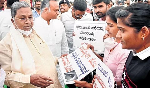 Siddaramaiah and Priyank Kharge interact with aspirants of state competitive exams who are demanding a speedy inquiry into the police sub-inspector recruitment scam, in Bengaluru on Tuesday | Express