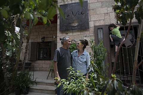 Kenae Totah, 5, right, plays while his parents Morgan Cooper, 41, center and foreign spouse Saleh Totah, right, pose for a photo in front of their restaurant in Ramallah. (Photo | AP)