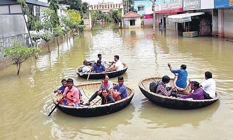 People wade through a flooded road on coracles off Sarjapur Road, in Bengaluru on Wednesday