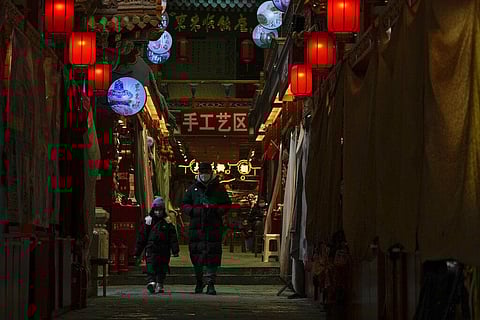 A man and a child wearing face masks walk by shuttered stores on Jan. 3, 2023, which would be selling souvenirs in Qianmen, a popular tourist spot in Beijing. (Photo | AP)