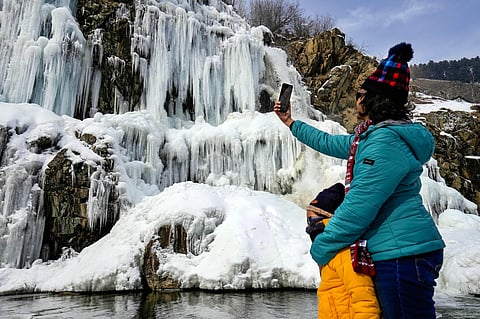 A tourist clicks a picture of a frozen waterfall at the Drung area of Tangmarg in Baramulla district of north Kashmir, on Jan. 18, 2023. (Photo | PTI)