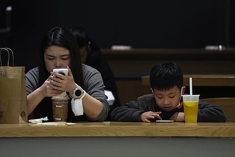 A woman and child check on their smartphones at a cafe in Beijing. (Photo | AP)