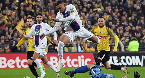 Paris Saint-Germain's French forward Kylian Mbappe jumps over Pays de Cassel's goalkeeper Romain Samson on his way to scoring a goal during the French Cup. (Photo | AFP)