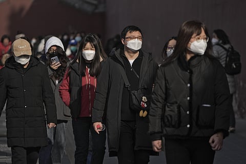 People wearing face masks walk along a street in Beijing. (Photo | AP)