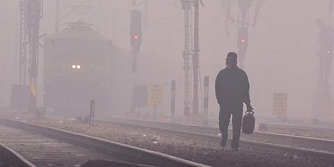A man walks along railway tracks during a cold and foggy morning. (Photo | PTI)