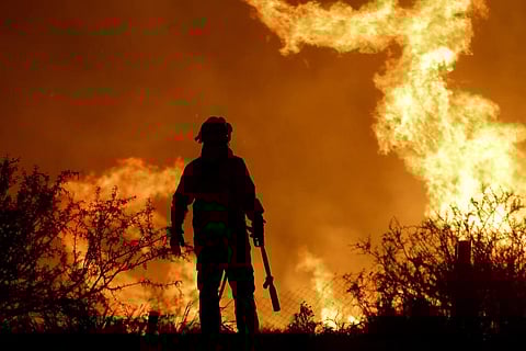 A firefighter is silhouetted by the flames of a forest fire on the outskirts of Villa Carlos Paz, Argentina, Tuesday, Oct. 10, 2023. (Photo | AP)