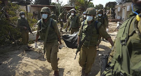 Israeli soldiers carry the body of a person killed in the Hamas attack in kibbutz Kfar Azza. (Photo | AP)