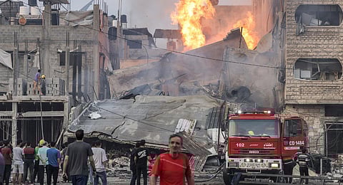 People watch as a firetruck is deployed outside a burning collapsed building following Israeli bombardment in Gaza City. (Photo | AFP)