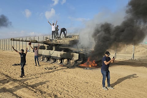 Palestinians celebrate by a destroyed Israeli tank at the Gaza Strip fence east of Khan Younis Saturday, Oct. 7, 2023. (Photo | AP)