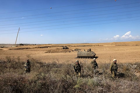 Israeli soliders walk in the bushes near their armoured vehicles stationed close to the border with the Gaza Strip on October 15, 2023. (Photo | AFP)