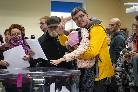 A voter flashes a victory sign after casting his ballot with the help from a child in Warsaw, Poland, Sunday, Oct 15, 2023. (Photo | AP)