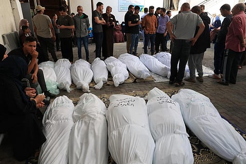Palestinian relatives stand with bodies wrapped in funeral shrouds with their names written for identification, at a hospital following Israeli military attacks on Rafah. (Photo | AFP)