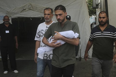 A Palestinian carries a child killed in the Israeli bombardment of the Gaza Strip in Rafah. (Photo | AP)