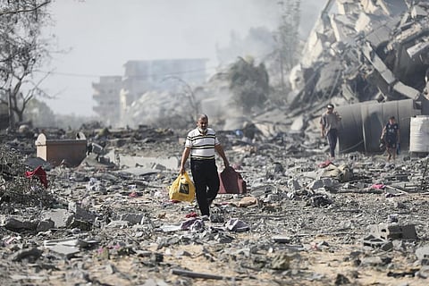 Palestinians walk by buildings destroyed in the Israeli bombardment on al-Zahra, on the outskirts of Gaza City. (Photo | AP)