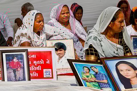 Family members holding pictures of relatives who lost their lives in the Morbi bridge collapse, stage a protest on the first anniversary of the incident, in Ahmedabad. (PTI)