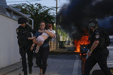 Police officers evacuate a woman and a child from a site hit by a rocket fired from the Gaza Strip, in Ashkelon, southern Israel, Saturday, Oct. 7, 2023. (Photo | AP)