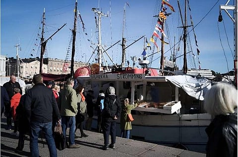 People crowd around the fishing boats in Helsinki harbor to buy fresh herring. (Photo | AFP)