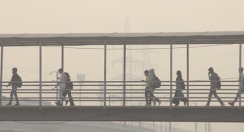 Commuters walk throw a foot-over bridge amid smog, in Gurugram.(Photo | PTI)