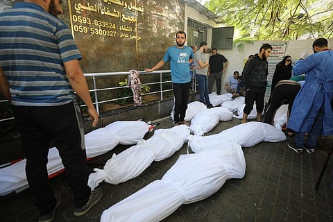 People stand by the wrapped bodies of victims who were killed in Israeli bombardment as they lie outside Al-Shifa hospital in Gaza City. (Photo | AFP)
