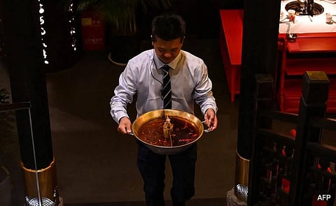 This photo taken on October 21, 2023 shows a restaurant employee taking away a pot of oily broth, which will be recycled, at an eatery in Chengdu. (AFP)