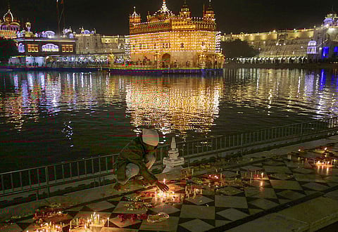 A devotee lights a candle at Golden Temple on Guru Nanak Jayanti, in Amritsar. (Photo | PTI)