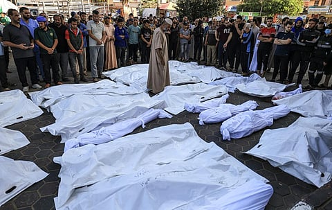 A man walks between the bodies wrapped in shrouds of those killed in Israeli bombardment in Deir Balah in the central Gaza Strip. (Photo | AFP)