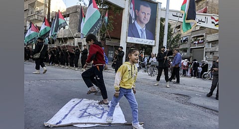 Children walk on a makeshift Israeli flag strewn on the ground past Palestinian members of the Saraya al-Quds. (Photo | AFP)