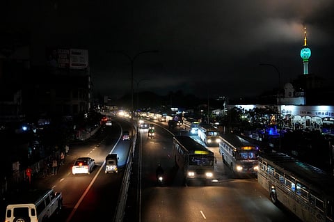 Vehicles move on a road past buildings partially lit during a countrywide power outage in Colombo, Sri Lanka, Saturday, Dec. 9, 2023 | AP