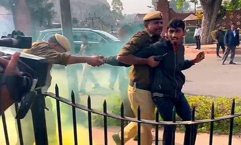 Police apprehend a man carrying a can emitting yellowish smoke while he was protesting outside the Parliament, during the Winter session, in New Delhi, Wednesday, Dec. 13, 2023. (PTI Photo)