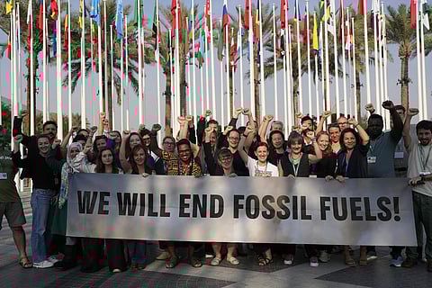 Members of Greenpeace gather for a photo around a sign that reads 'We will end fossil fuels' at the COP28 U.N. Climate Summit in Dubai (Photo | AP)
