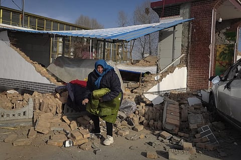 A woman collects clothes from her damaged home after the earthquake in Jishishan county, in northwest China's Gansu province. (Photo | AP)