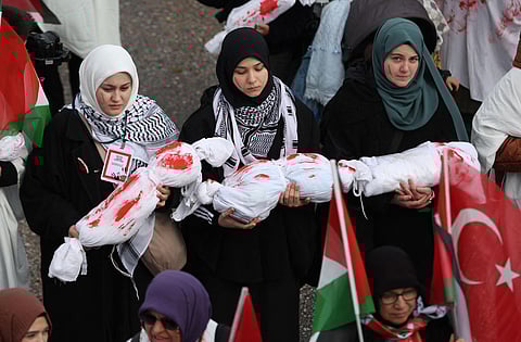 Protesters carry wrapped dolls covered with red paint during a rally in solidarity with the Palestinians in Gaza, in Ankara on December 24, 2023. (AFP)