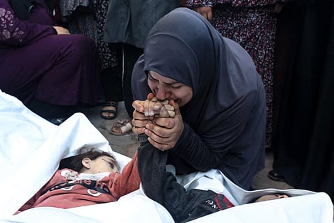 Mother of twins Ahmed and Jihan Nasser, who were killed during Israeli bombardment, kisses their hands as she mourns over their bodies at Al-Aqsa hospital in Deir al-Balah in central Gaza | AFP
