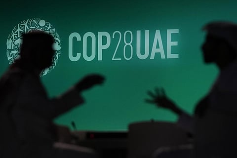 People are silhouetted against a logo for the COP28 UN Climate Summit on November 29, 2023, in Dubai, United Arab Emirates. (File photo | AP)