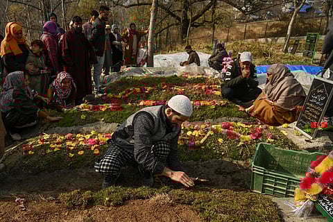 A relative places a patch of grass over the grave of a slain militant at a graveyard in Waddur village, in northern Kashmir. (Photo | AFP)