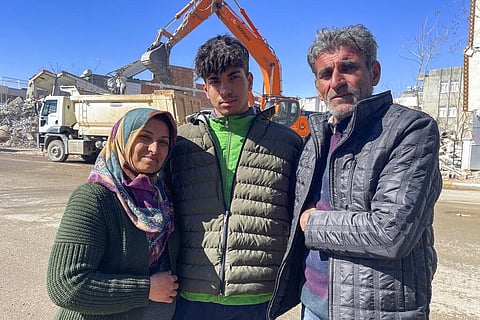 Taha Erdem (C) poses for a photograph with his parents next to the destroyed building where he was trapped after the earthquake in Adiyaman, Turkey. (Photo | AP)